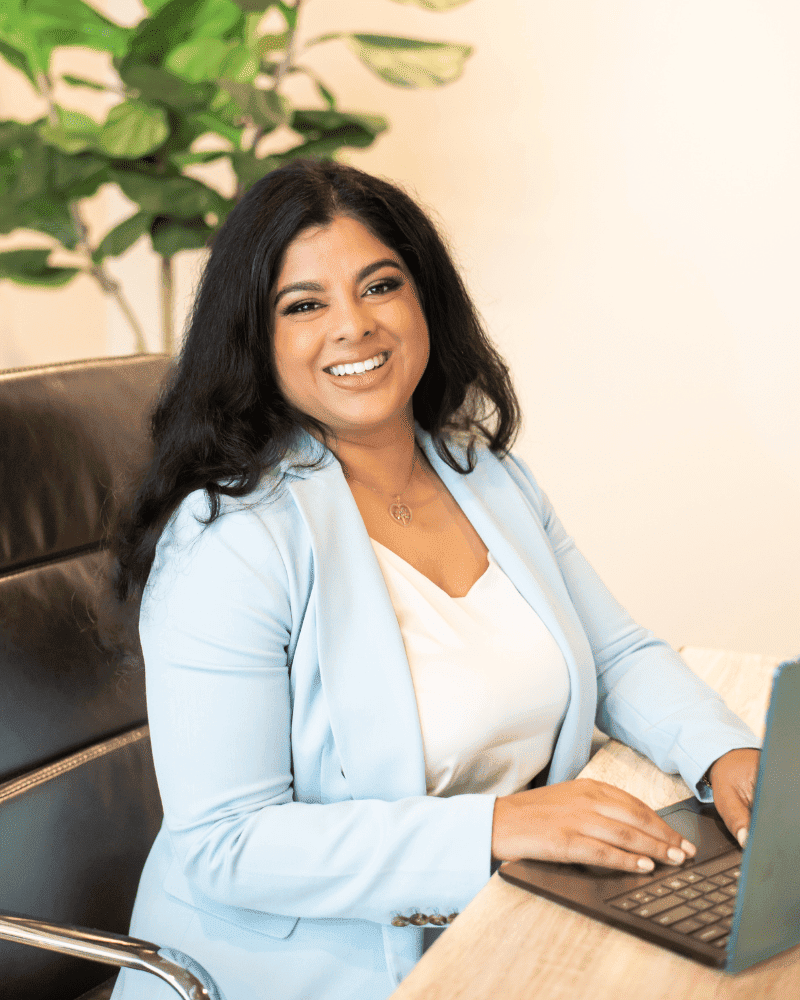 Professional Nadia Ramsaran Smiling And Sitting At A Desk With A Laptop