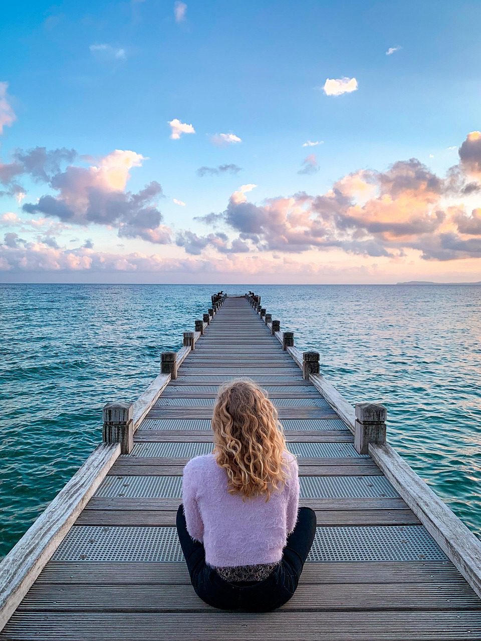 woman on sitting a jetty by a calm sea 