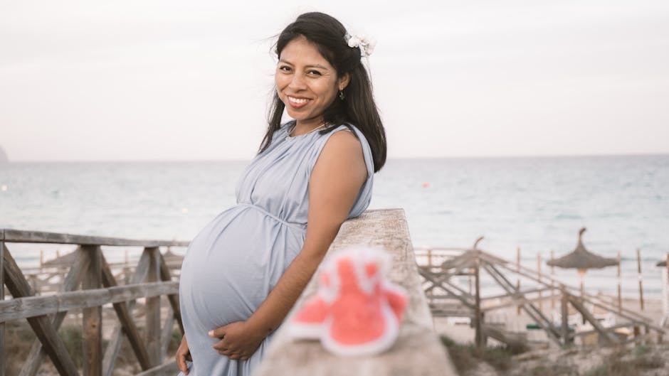 Asian woman in maternity dress smiling by the beach with baby shoes.